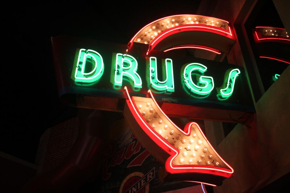 neon sign saying "drugs" with an arrow