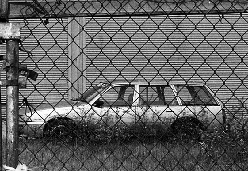 black and white photo of a station wagon behind chain link fencing