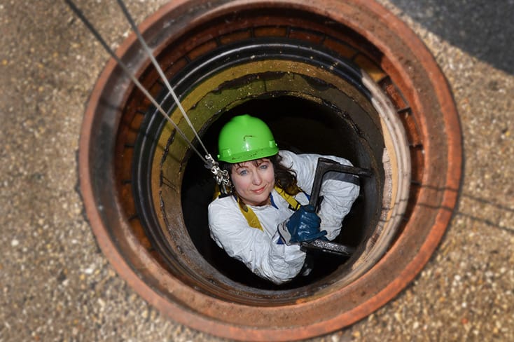 woman in a green hard hat climbing into a manhole